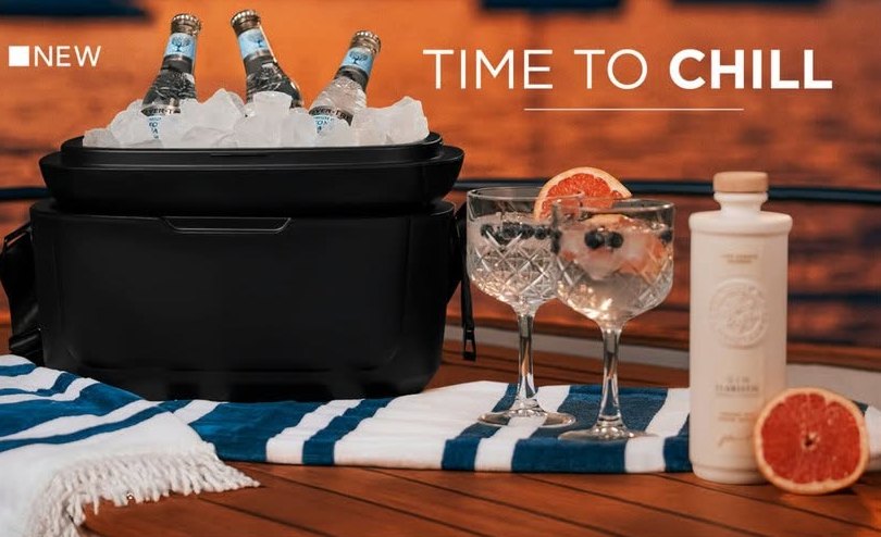 Black cooler box filled with ice and bottles beside cocktail glasses