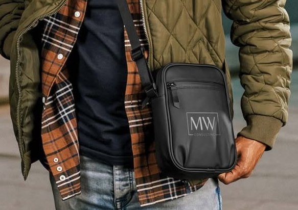 Black crossbody bag with a company logo worn over a padded jacket